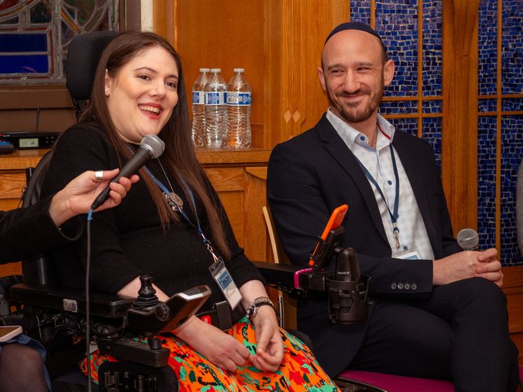 Two panellists holding microphones in conversation, one of them seated in a wheelchair