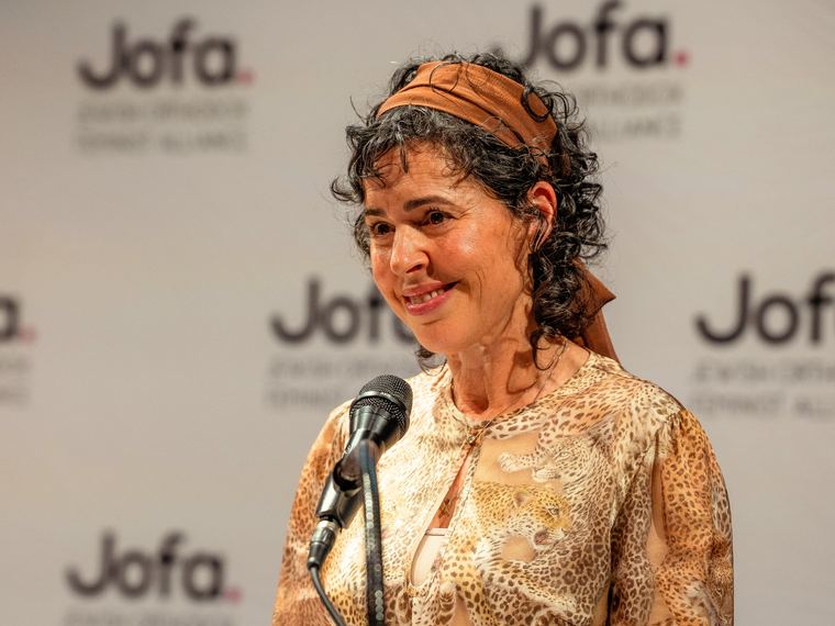 A woman speaking into a microphone in front of a Jofa backdrop