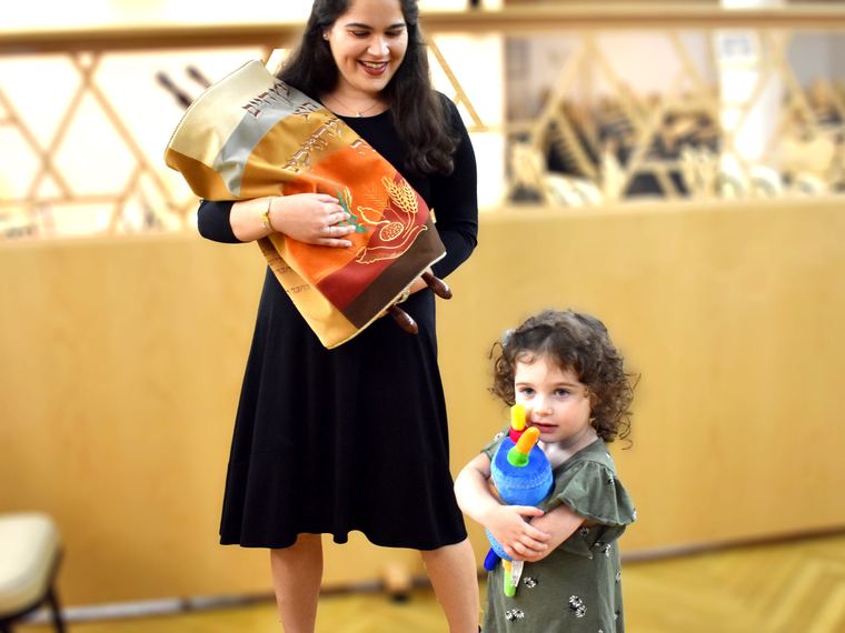A woman carrying a Torah scroll, walking beside a young child