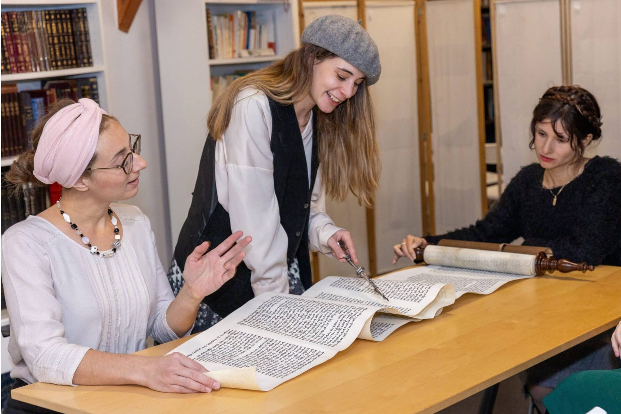 Women reading from a Torah scroll together with a yad in a study library