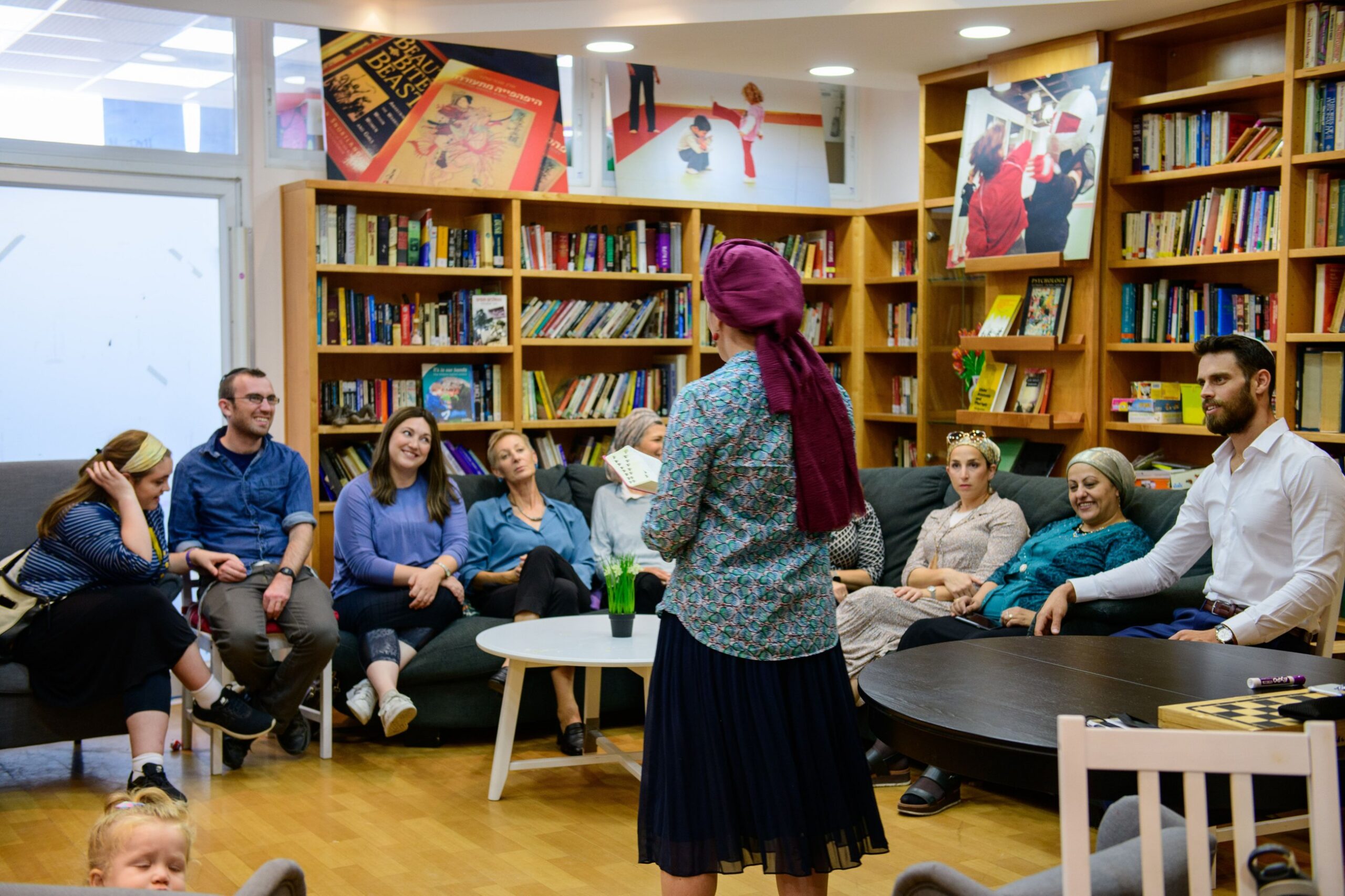 A woman teaching Torah to a seated group in a library