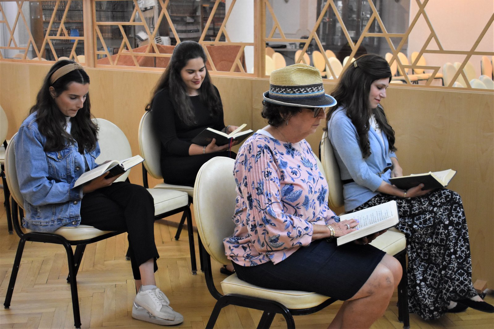 Four women seated in a sanctuary, each davening from an open siddur