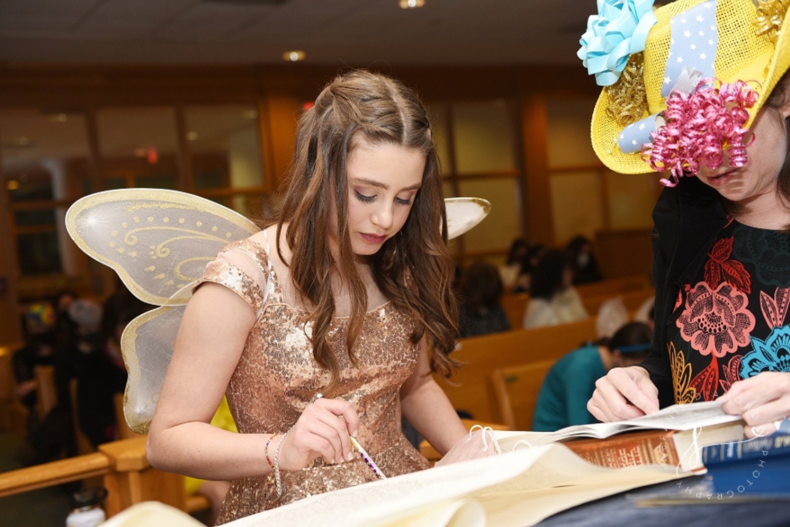 A girl in a Purim costume reading from a Megillah scroll alongside another reader