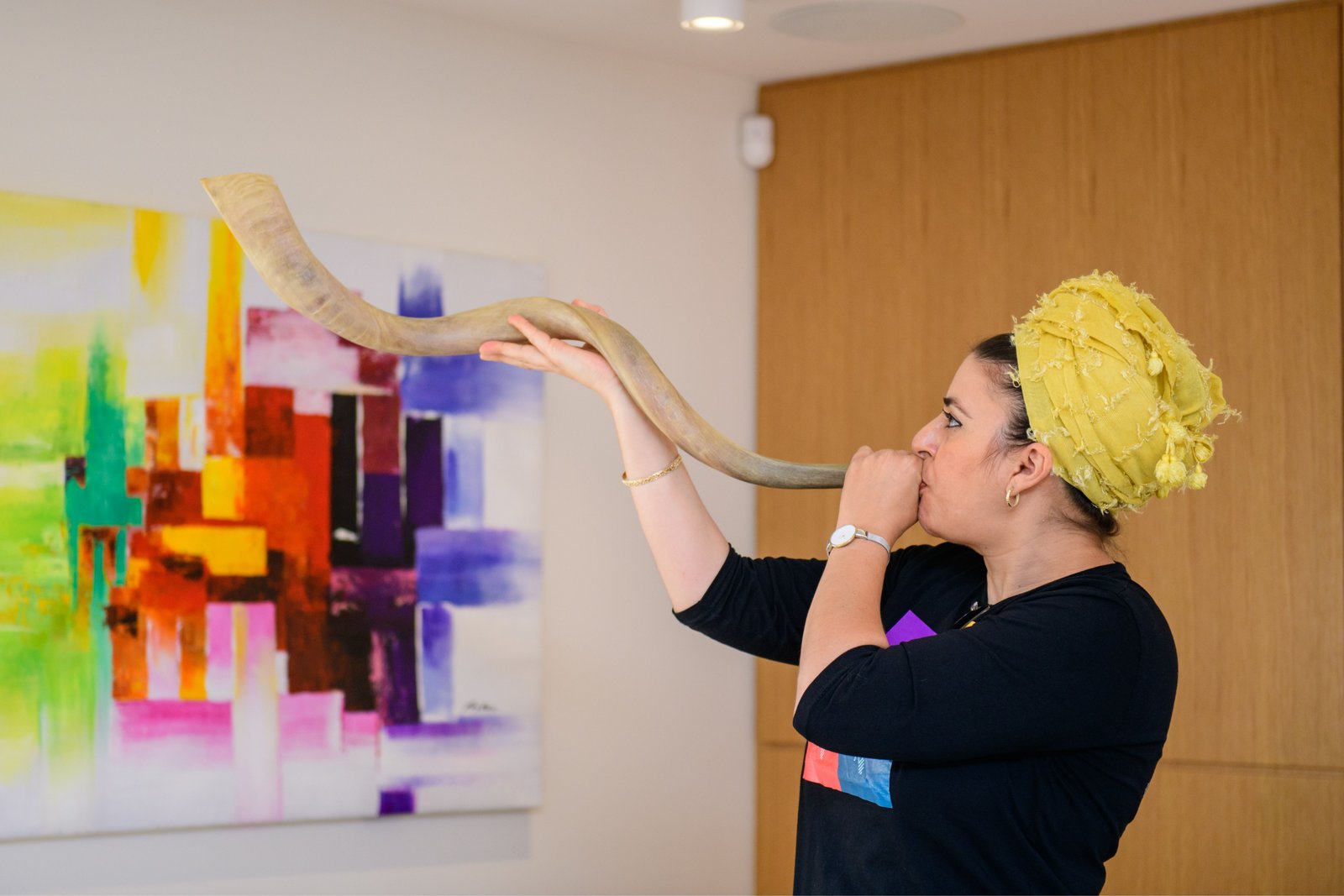 A woman in a yellow headscarf blowing a long curved shofar
