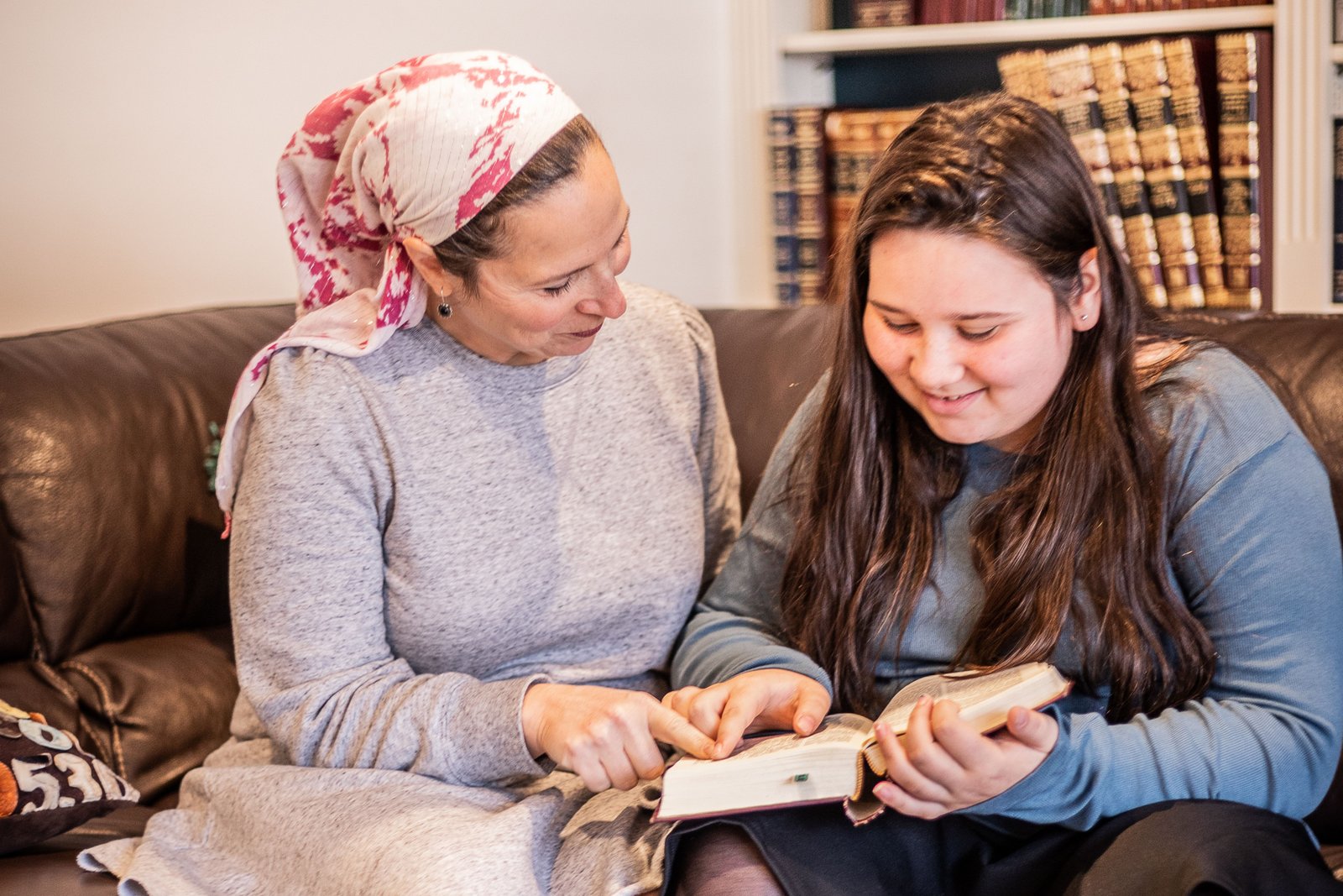 A woman and a teenage girl sitting together on a couch, learning from an open siddur